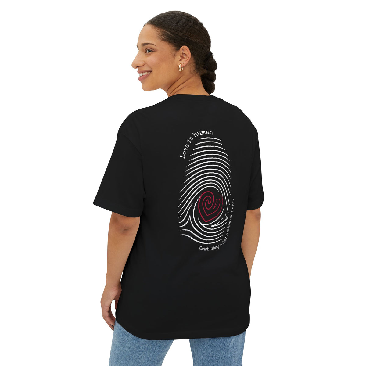 A woman shown from the back wearing a black short-sleeve T-shirt,  featuring a graphic print of a fingerprint with a red heart center and text reading 'Love is human' and 'Celebrating what makes us human'.