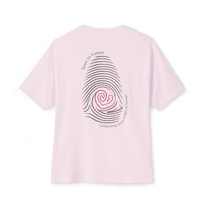A light pink  short-sleeve t-shirt shown from the back, featuring a graphic print of a fingerprint with a red heart center and black text reading 'Love is human' and 'Celebrating what makes us human'.