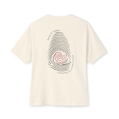 An off-white short-sleeve t-shirt shown from the back, featuring a graphic print of a fingerprint with a red heart center and black text reading 'Love is human' and 'Celebrating what makes us human'.