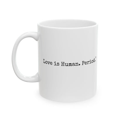 A white ceramic coffee mug with black printed text reading 'Love is Human. Period.