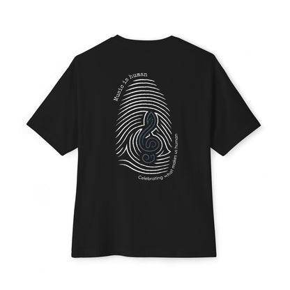 A black short-sleeve t-shirt shown from the back, featuring a large graphic print of a fingerprint made of sound waves with a musical clef symbol in the center, surrounded by white text that reads 'Music is human' and 'Celebrating what makes us human