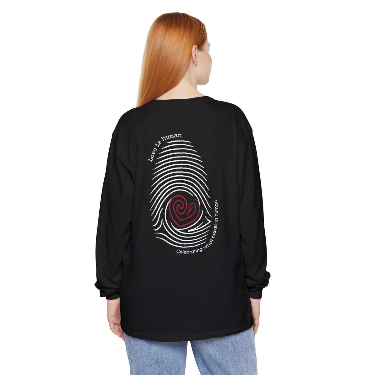 A woman with red hair is shown from the back wearing a black long-sleeve t-shirt with a large multicolor spiral fingerprint graphic and text on the back, paired with light blue jeans, against a plain white background. 