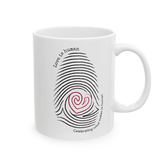 A white ceramic mug featuring a black fingerprint graphic with a red heart at the center and the text 'Love is human' and 'Celebrating what makes us human'.