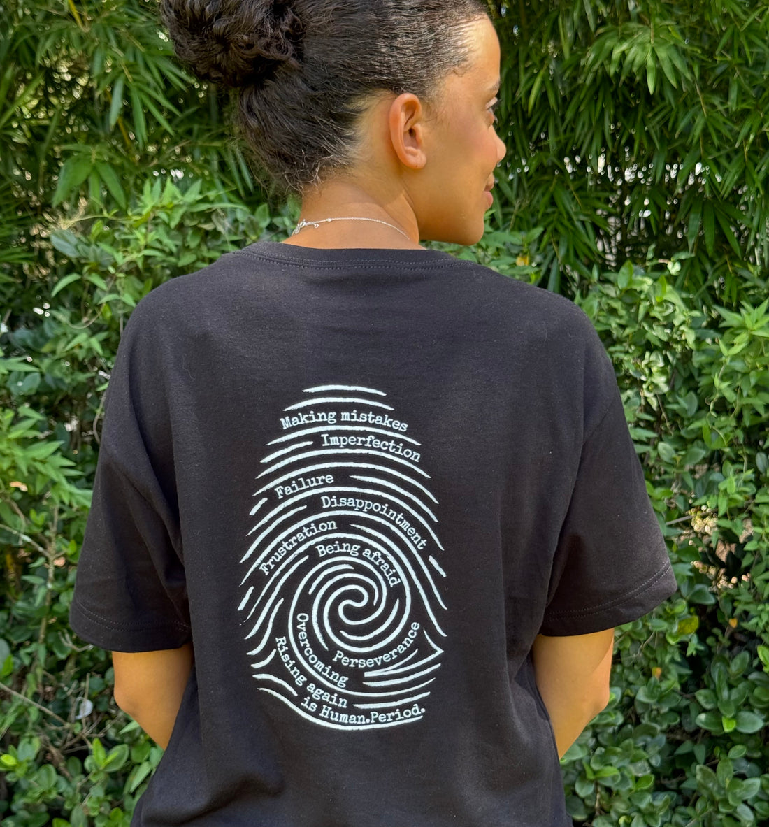 Black t-shirt  with a white fingerprint.  The words making mistakes, imperfection, failure, disappointment, frustration, being afraid, overcoming, perseverance and rising again is human.period. is embedded in the fingerprint.  