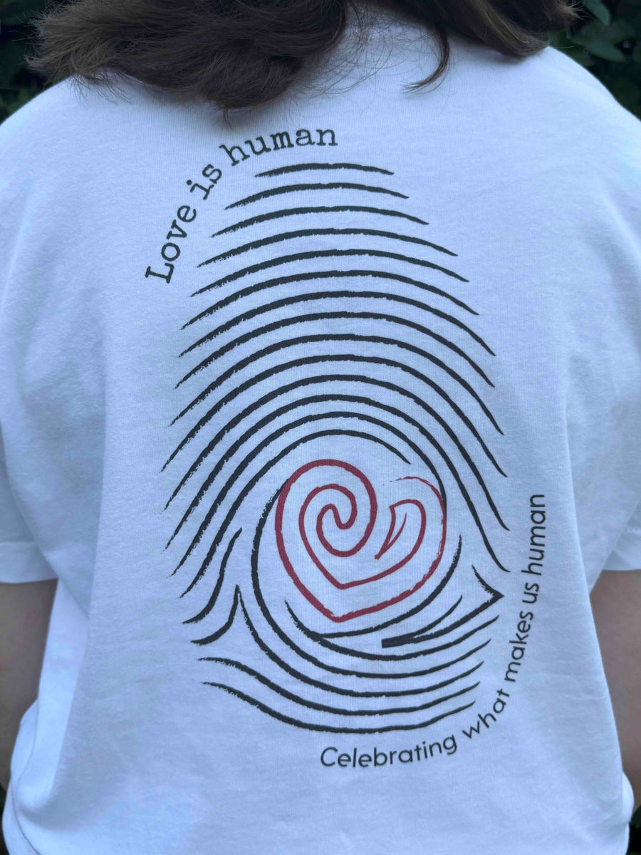 White t-shirt with Love is human and celebrating what makes us human text.  A fingerprint design with a red heart in the middle. 